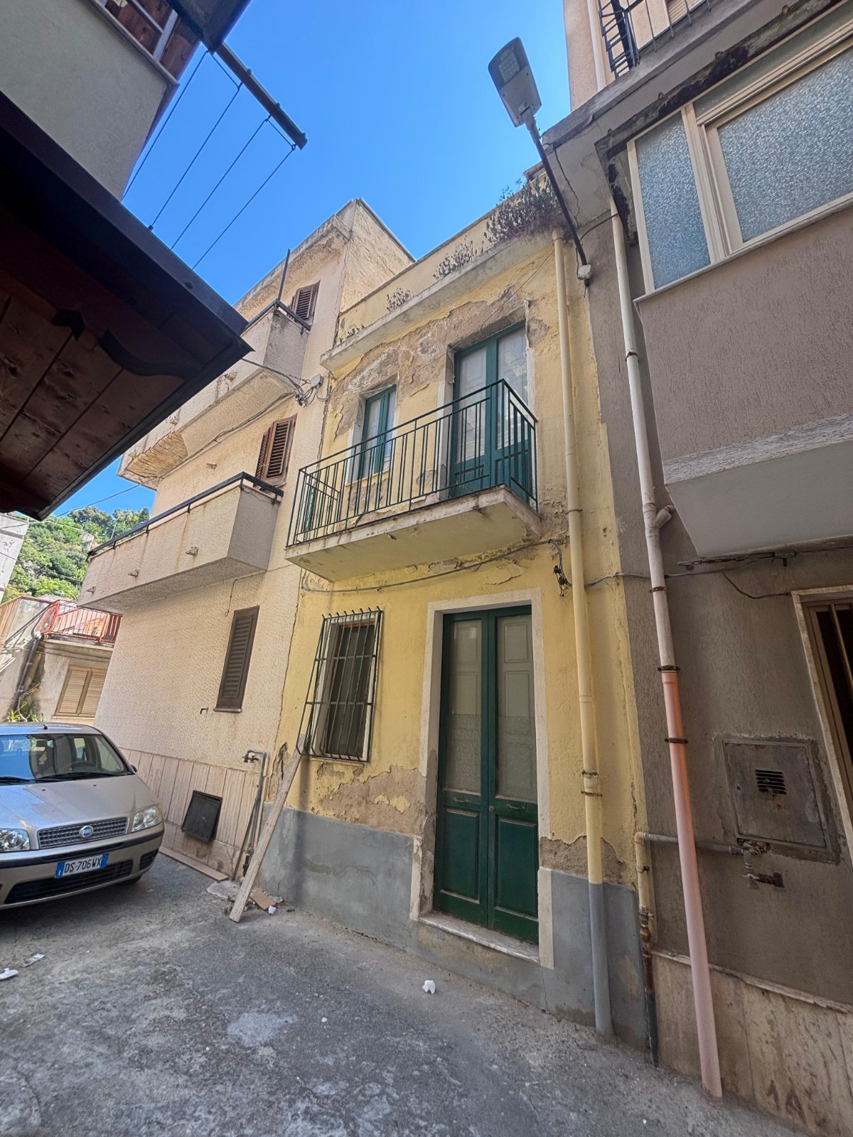 Prima: facciata esistente con intonaco deteriorato, serramenti verdi e balcone